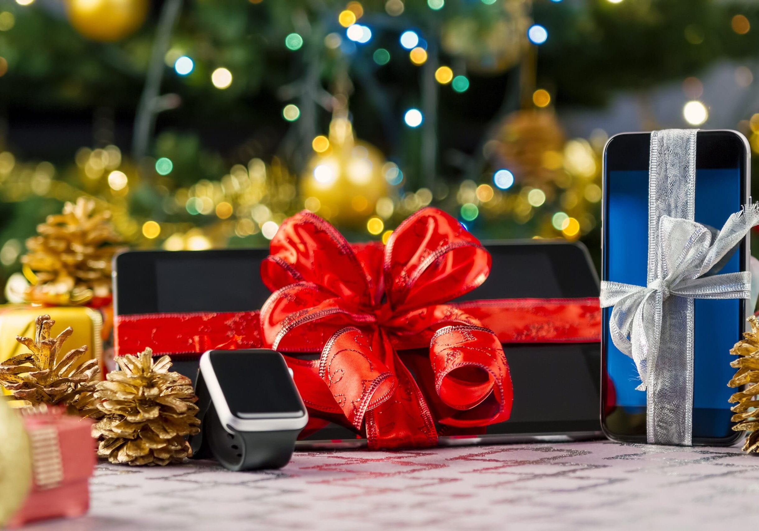 Tablet pc, smartphone and smartwatch with gifts and decorations in front of Christmas tree. Focus on smartphone.